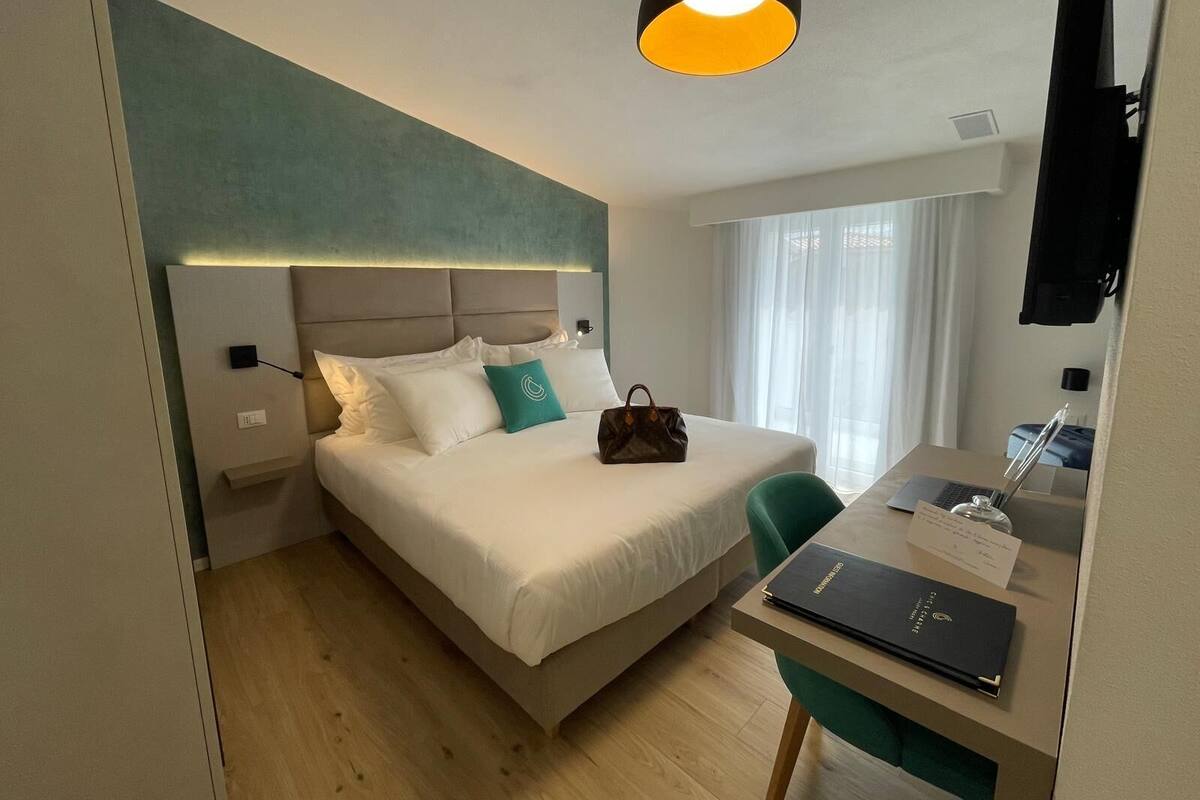 Een hotelkamer met een bed, een bureau met een laptop, een handtas en een televisie aan de muur.
