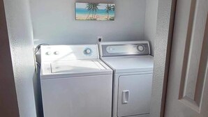 Un espace buanderie avec deux machines à laver et deux sèche-linge superposés, une porte en bois et un petit tapis sur le sol.