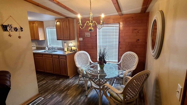 Une cuisine chaleureuse avec des meubles de rangement en bois, une table à manger en verre, des chaises en osier et un lustre.