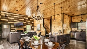 Une cuisine moderne aux murs en bois, un coin repas avec une table et des chaises en bois, et un grand lustre.