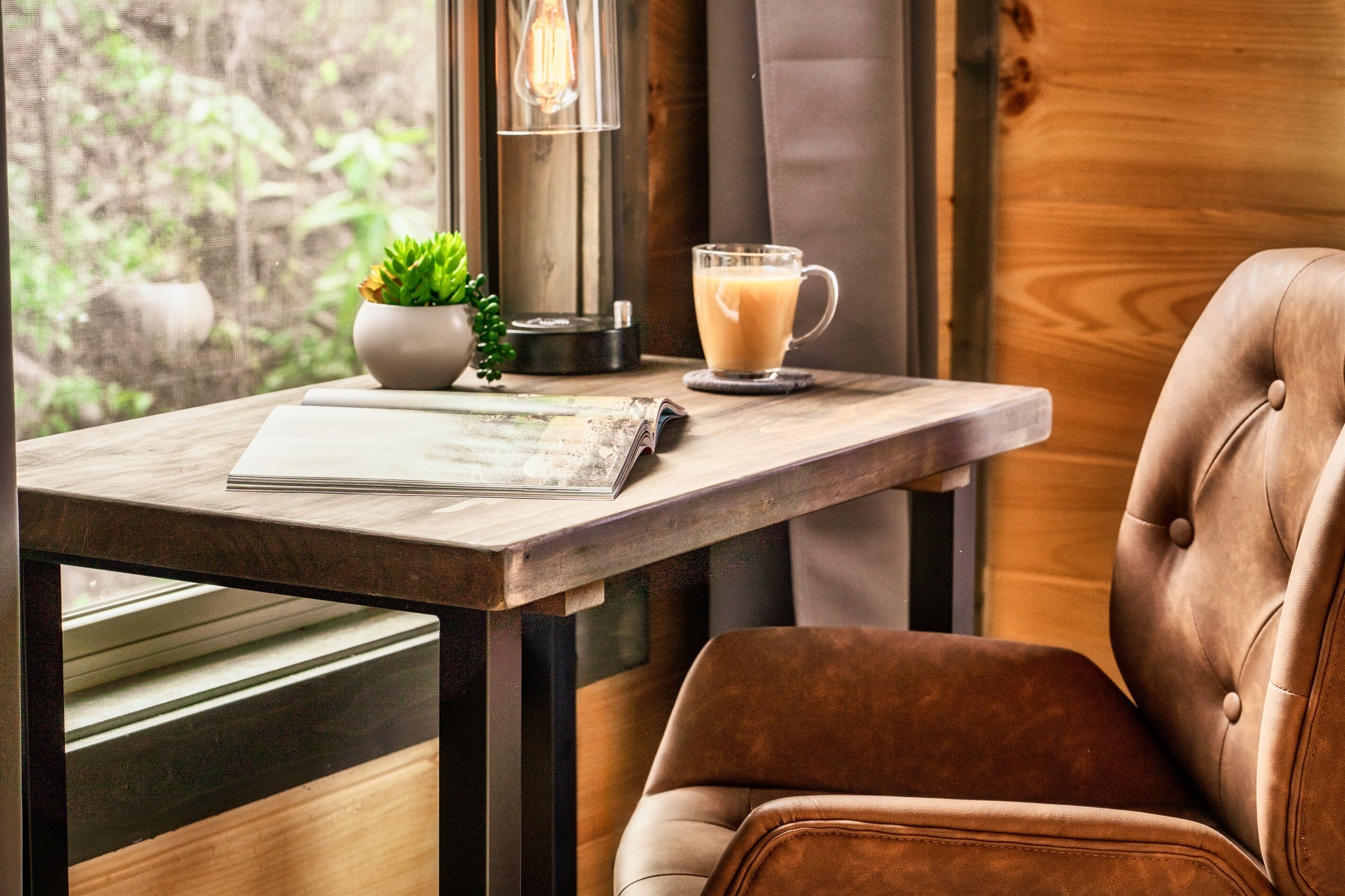 A cozy seating area with a leather chair, a table with a glass mug of coffee, a small potted plant, and a lamp.