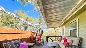 A covered porch with outdoor furniture, a wooden fence, and a view of trees.