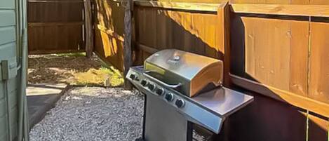 Een achtertuin met een barbecue en een houten omheining.