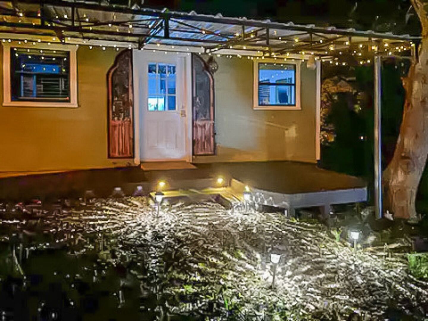 A covered outdoor area with a bench, string lights, and a door leading to a building.