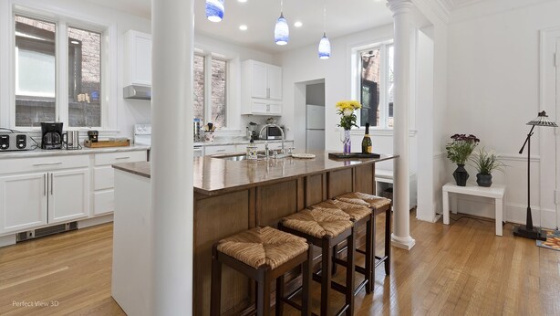 Una cucina moderna con mobili bianchi, un'isola in legno con sgabelli da bar e luci a sospensione.