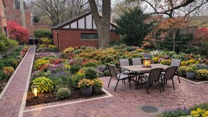 Un patio in mattoni con tavolo e sedie, circondato da una varietà di fiori colorati.