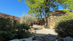 A rustic stone building with a tiled roof, surrounded by lush greenery and a gravel path. - Maison Nina: un Ancien Corps de Ferme Rénové Avec Piscine, Entre Dordogne et Lot (CAMPAGNAC LES QUERCY)