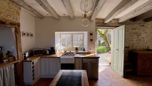 A rustic kitchen with exposed beams, a large window, and a view of the garden. - Maison Nina: un Ancien Corps de Ferme Rénové Avec Piscine, Entre Dordogne et Lot (CAMPAGNAC LES QUERCY)