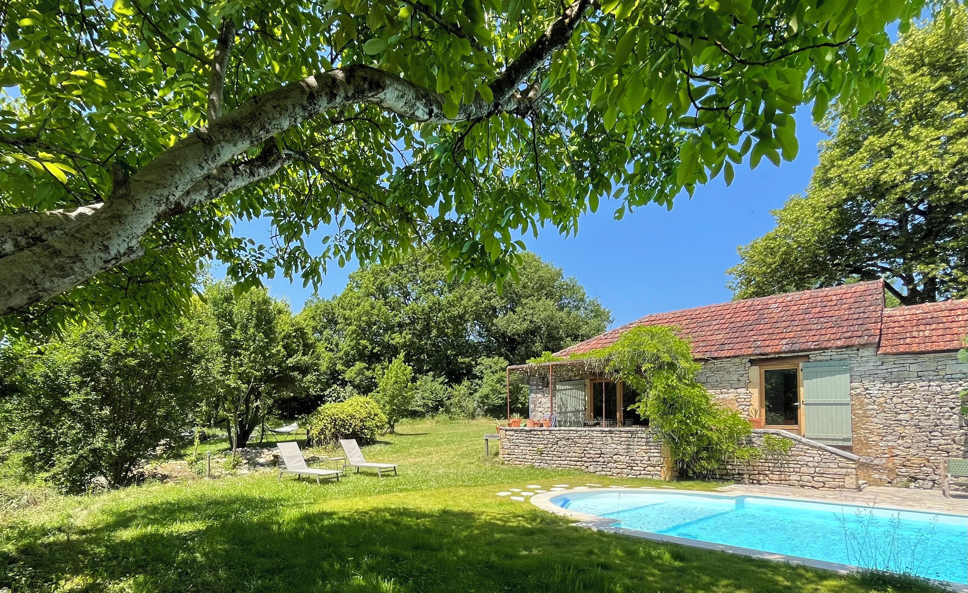 Un bâtiment en pierre doté d’une piscine, entouré d’une végétation luxuriante et d’arbres.