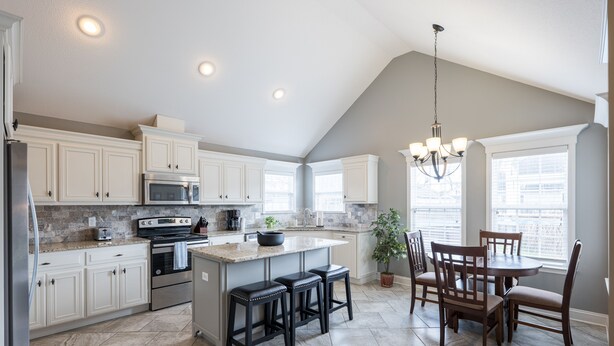 A kitchen with white cabinets, a large island, a dining area with wooden chairs, and a chandelier. - Peaceful Retreat on Newbury with Pool, Soaking Tub, King Bed (Valdosta)