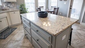 A kitchen with granite countertops, white cabinetry, and a dining area with a table and chairs. - Peaceful Retreat on Newbury with Pool, Soaking Tub, King Bed (Valdosta)