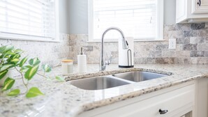 A kitchen with a granite countertop, stainless steel sink, and white cabinetry. - Peaceful Retreat on Newbury with Pool, Soaking Tub, King Bed (Valdosta)
