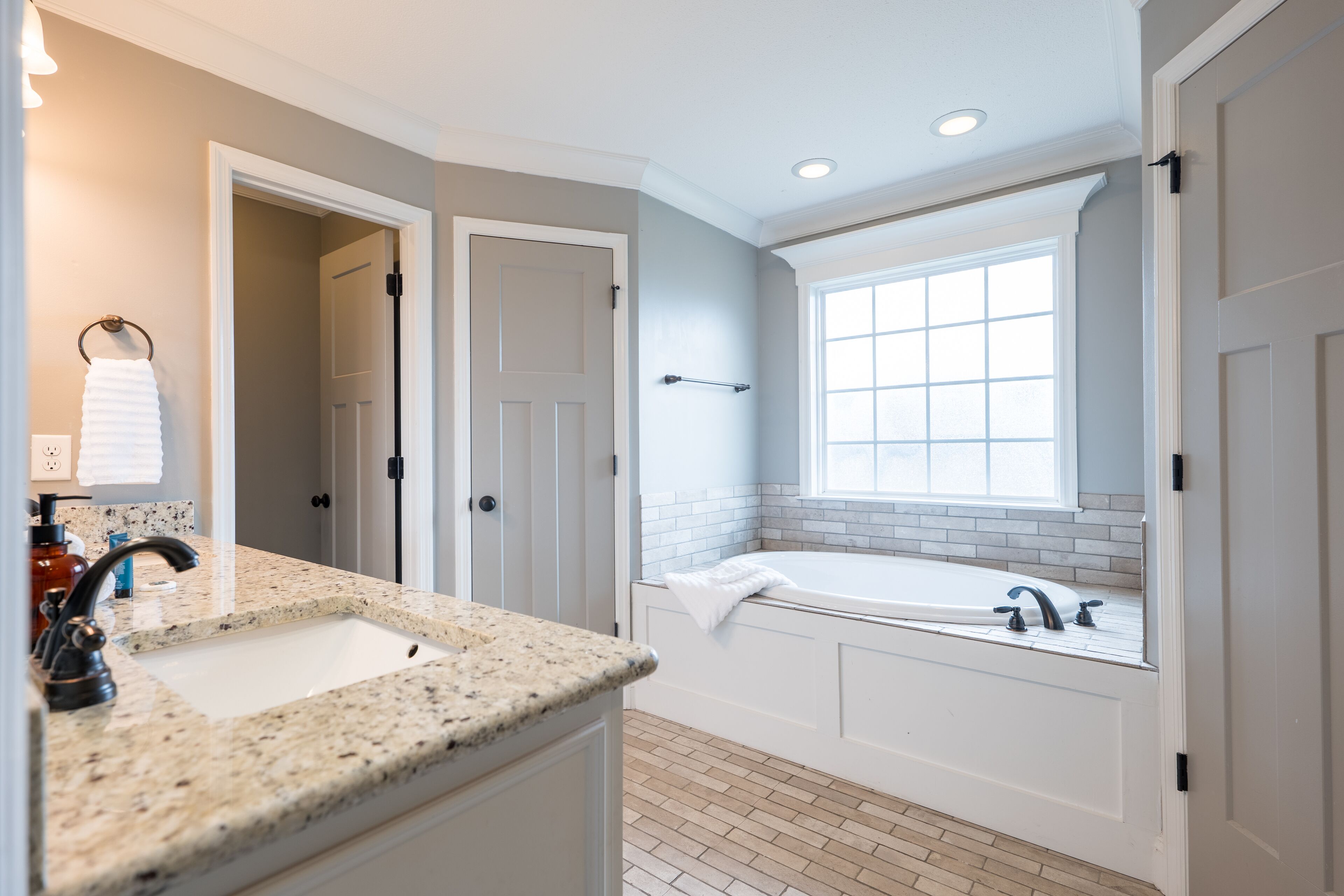 A modern bathroom with a granite countertop sink, a bathtub, and a window providing natural light.