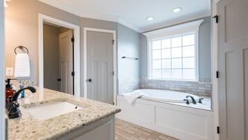 A modern bathroom with a granite countertop sink, a bathtub, and a window providing natural light.