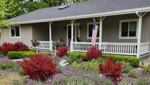 Ein eingeschossiges Haus mit Veranda, einer Flagge und einem gepflegten Garten mit verschiedenen Sträuchern und Blumen.