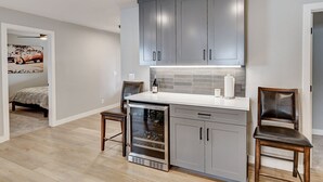 Eine moderne Küche mit grauen Schränken, einem eingebauten Backofen und einem Weinkühlschrank. Zwei Holzstühle und ein kleiner Tisch ergänzen das Bild.