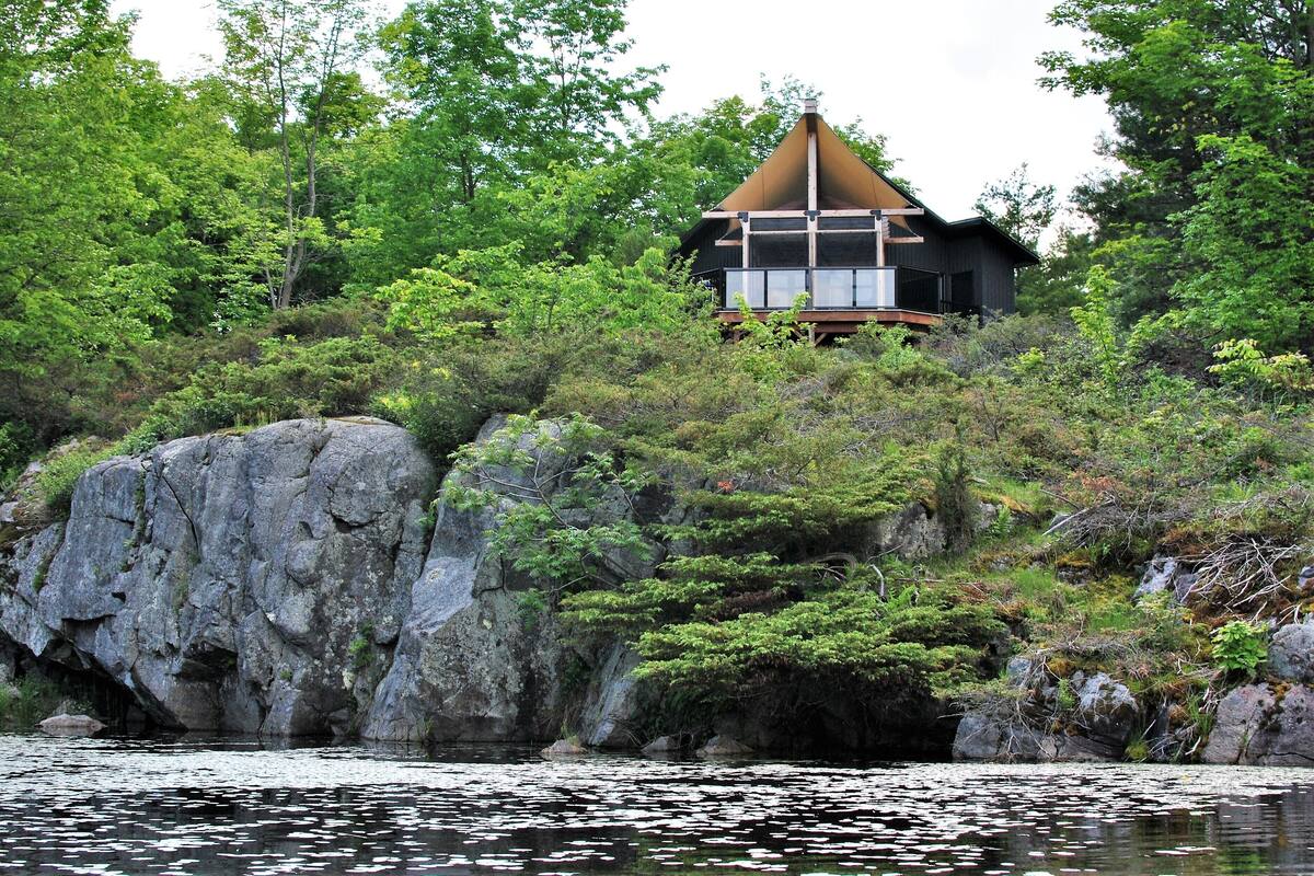 Una casa con techo triangular, rodeada de bosque denso y terreno rocoso.