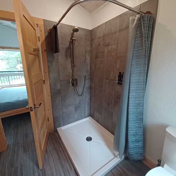 Una ducha con puerta de vidrio, una puerta de madera a la izquierda y una bañera blanca.