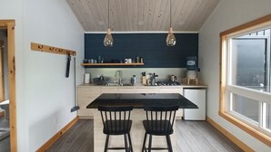 Une cuisine moderne dotée d’un îlot central, de deux tabourets de bar, d’un éclairage suspendu et d’une grande fenêtre.