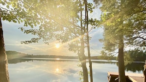 Une terrasse en bois, agrémentée de chaises Adirondack, donnant sur un lac paisible et entourée d’arbres.