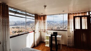 A room with a large window offering a cityscape view, a desk with a chair, and a bed. - SUMMIT VIEWPOINT HOUSE (Cusco)