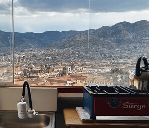 A kitchen with a sink, faucet, and stove, overlooking a cityscape with mountains in the background.