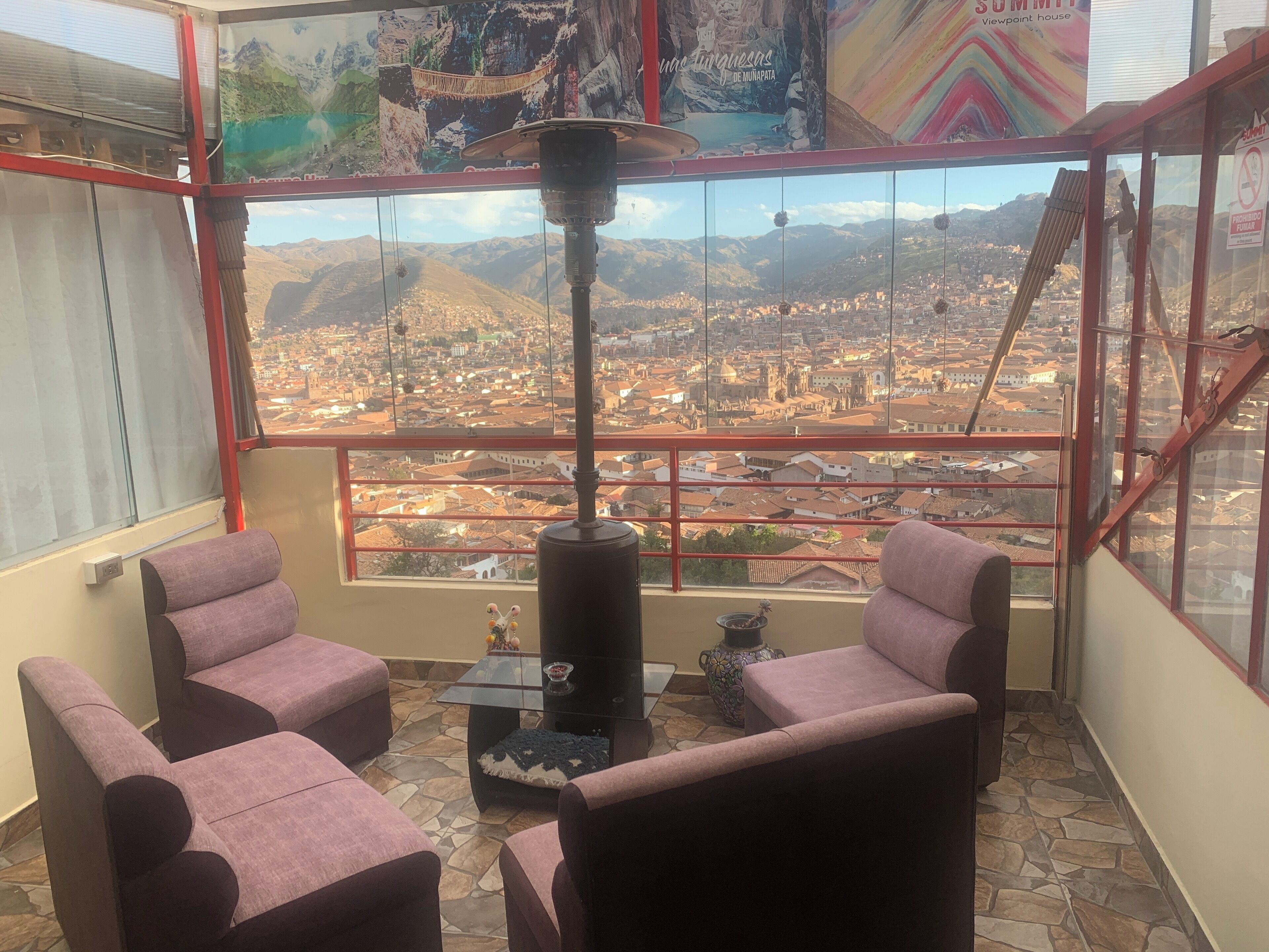 A balcony with a city view, two cushioned chairs, a table, a decorative vase, and a hanging lamp.
