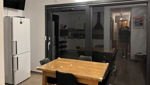 Une cuisine moderne dotée d’un four encastré, d’une table à manger avec des chaises et d’un téléviseur fixé au-dessus du réfrigérateur.
