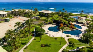 Vista aérea de um resort com várias piscinas, palmeiras e uma praia.