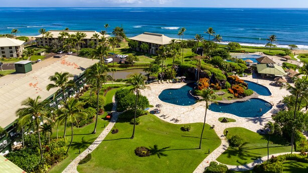 Luftaufnahme eines Resorts mit mehreren Schwimmbecken, Palmen und einem Strand.