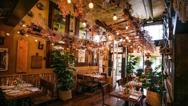 A cozy restaurant with wooden tables and chairs, hanging floral decorations, and potted plants. - Clean, Classy, Convenient. Montclair's Best Stay! Walk to town and train (Montclair)