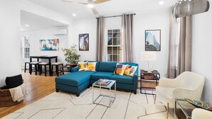 A modern living room with a sectional sofa, a glass coffee table, a white armchair, and a dining area with a table and chairs. - Clean, Classy, Convenient. Montclair's Best Stay! Walk to town and train (Montclair)