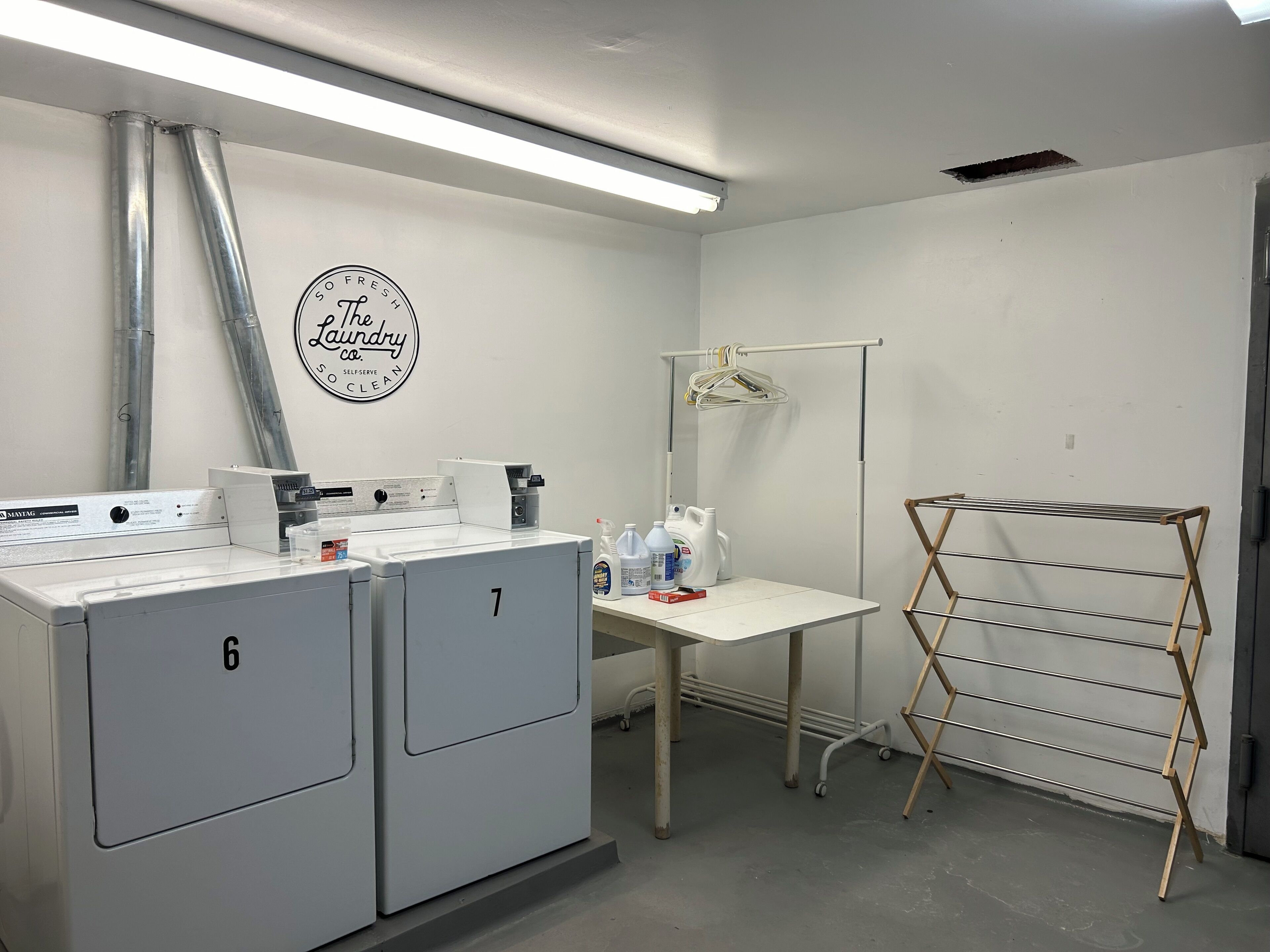 A laundry room with two large industrial washers, a drying rack, and a wall-mounted sign.
