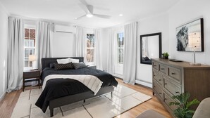 A modern bedroom with a bed, a dresser, a mirror, and a ceiling fan. - Clean, Classy, Convenient. Montclair's Best Stay! Walk to town and train (Montclair)