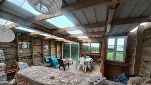A rustic wooden room with a high ceiling, skylights, a dining area with a table and chairs, and a view of the outdoors. - Waterfront gîte in a natural area at Lilia Plouguerneau. Sea view! (Plouguerneau)