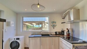 A modern kitchen with a built-in washer, a large window, and a hanging light fixture. - Waterfront gîte in a natural area at Lilia Plouguerneau. Sea view! (Plouguerneau)
