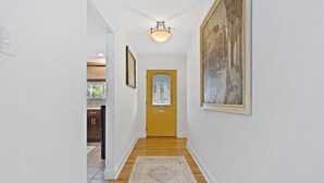 A hallway with a wooden floor, a rug, a yellow door, and a painting on the wall.