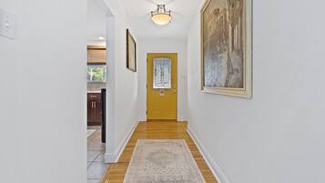 A hallway with a wooden floor, a rug, a yellow door, and a painting on the wall.