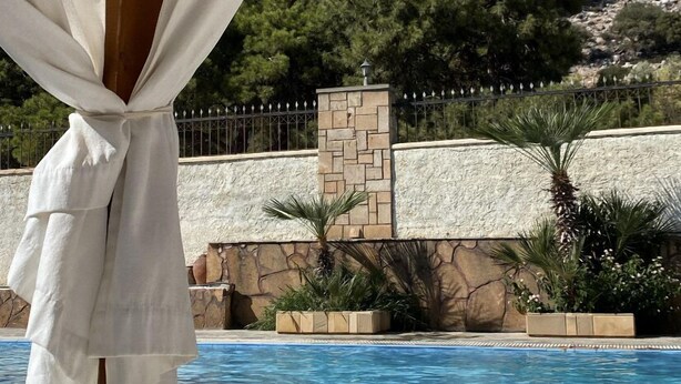 A poolside area with a view of a rocky mountain, a stone wall, and a palm tree. - Theonia Villas (Pefki)