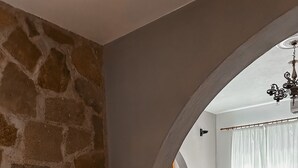 A room with a stone wall, a white statue, a dining area with a table and chairs, and a chandelier. - Theonia Villas (Pefki)
