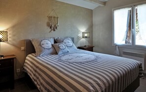 Quarto com colcha listrada, duas mesas de cabeceira com luminárias, um objeto pendurado na parede e uma janela com cortinas.