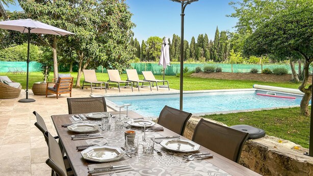 An outdoor dining area with a pool, lounge chairs, and a covered table.