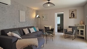 A living room with a grey sofa, a round coffee table, and two armchairs. There are wall-mounted artworks and a pendant light.