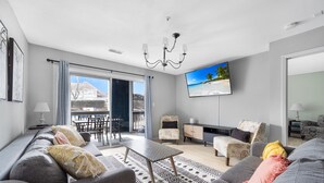 Una sala de estar moderna con un sofá, sillones, una mesa de centro y un televisor. Hay un balcón con vistas al mar.