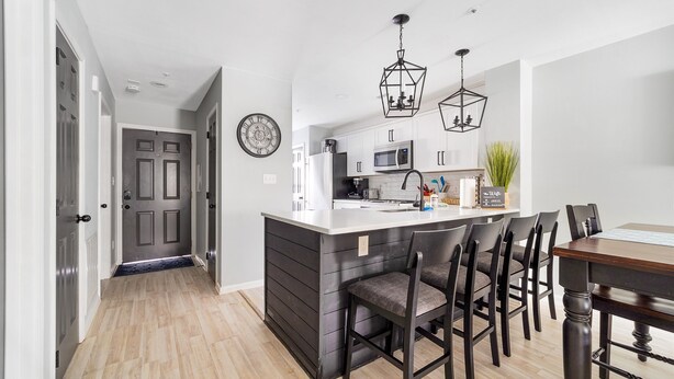 Una cocina moderna con una isla central, muebles oscuros y una zona de comedor con mesa y sillas de madera.