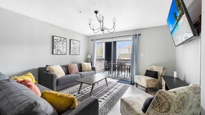 Una sala de estar moderna con un sofá gris, sillones estampados, una mesa de centro y un televisor de pantalla plana montado en la pared.