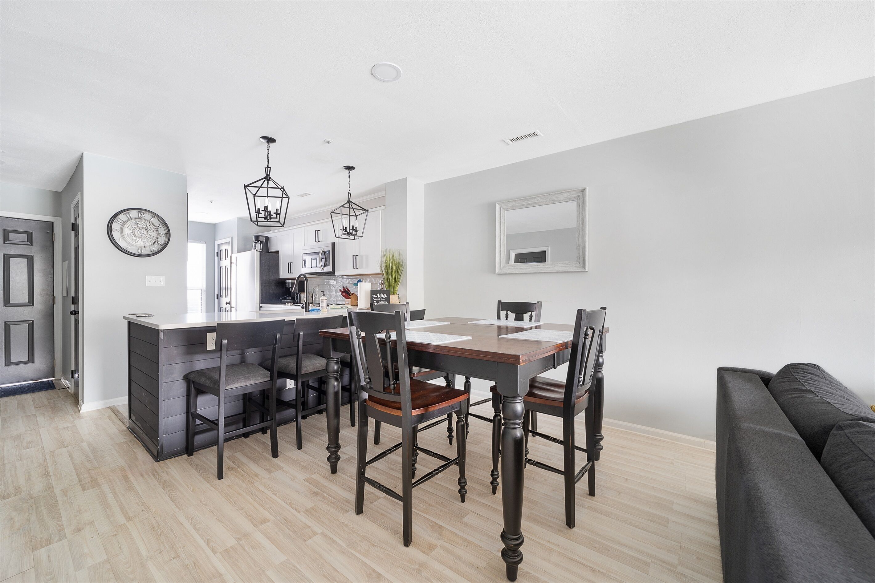 A modern kitchen with a dining area, wooden flooring, and a black sofa.