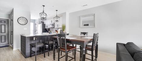 A modern kitchen with a dining area, wooden flooring, and a black sofa.