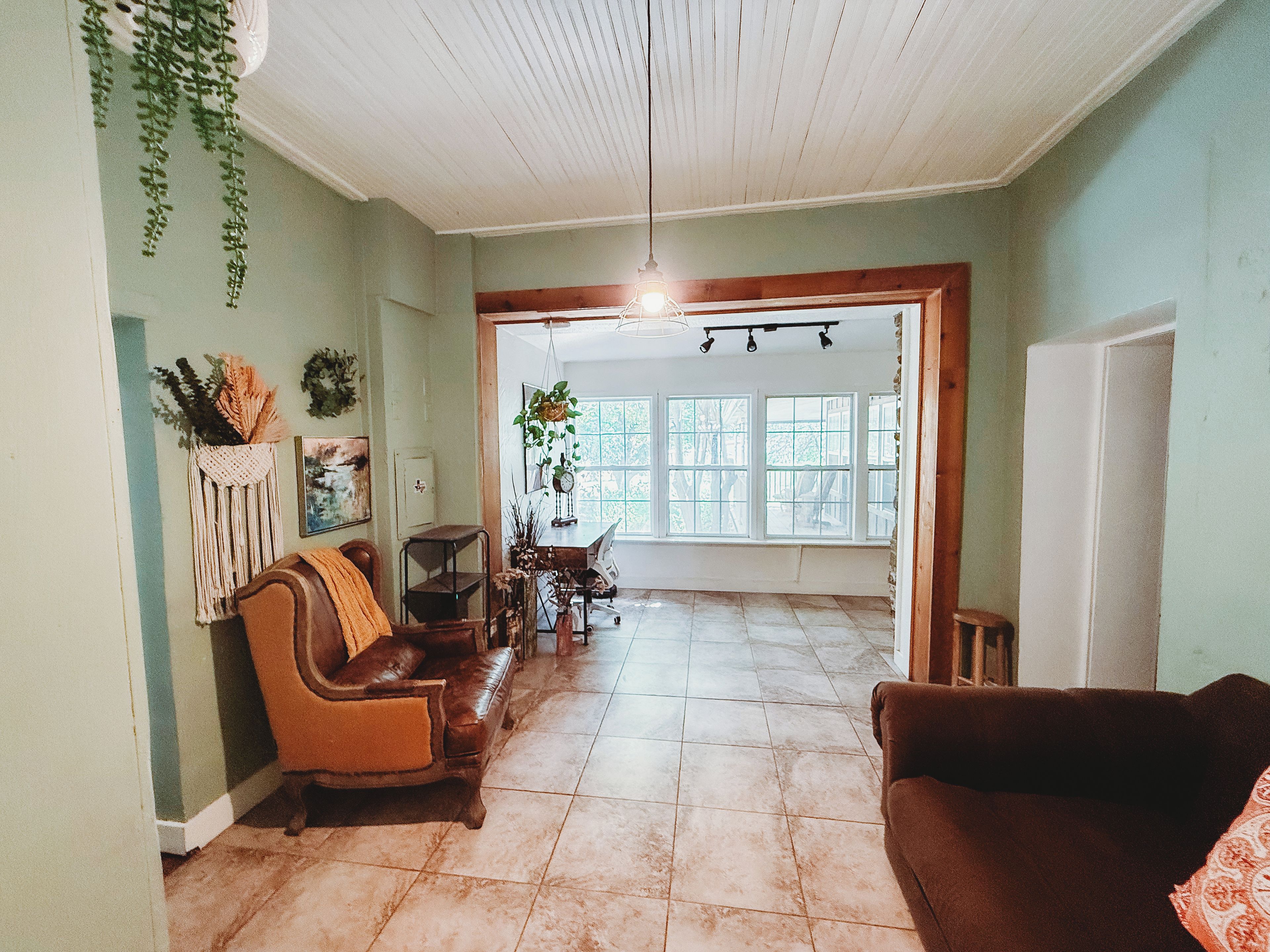 A spacious living area with a brown leather sofa, a wooden coffee table, and a hanging plant.