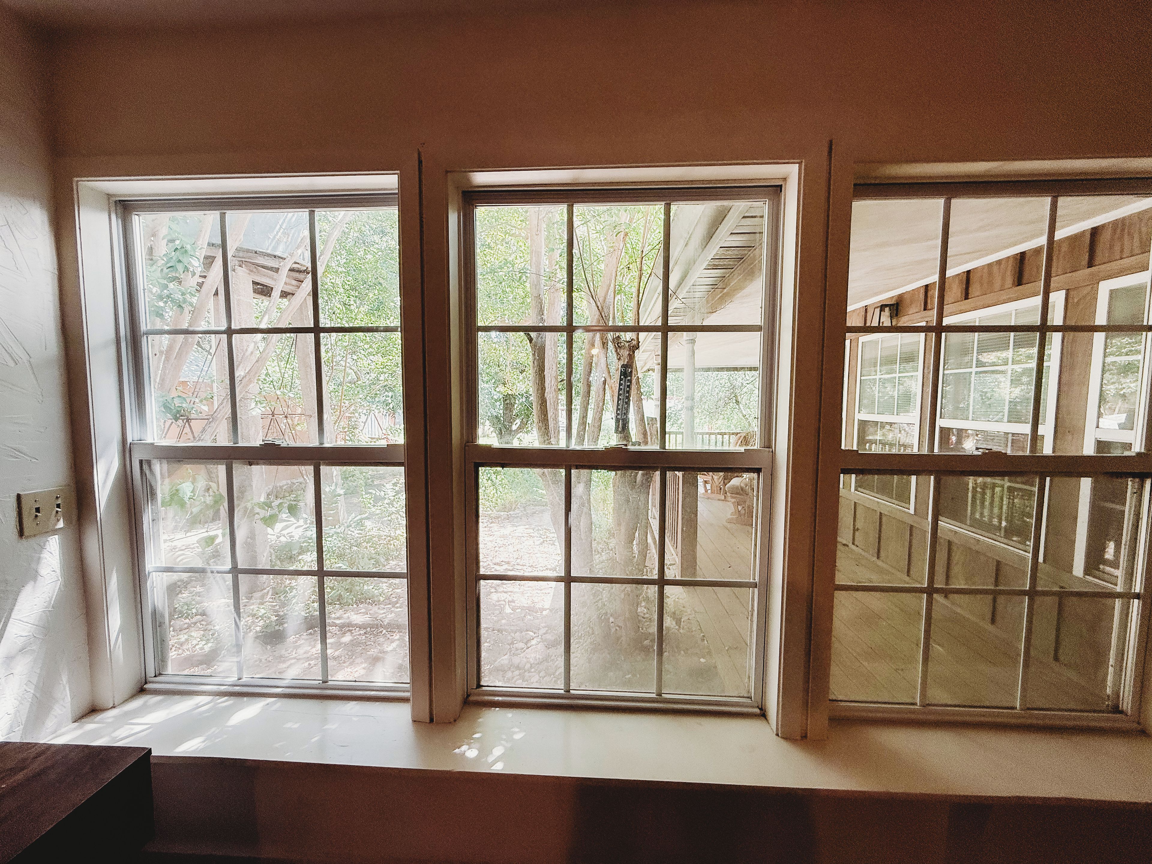 A room with three windows, each with a wooden frame and multiple panes, overlooking a wooden deck and outdoor area.